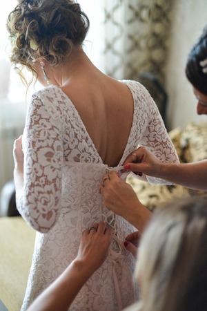 Garter on the leg of a bride, slim sexy bride in wedding luxury dress showing her silk garter with golden ribbon. woman have a final preparation for wedding ceremony. Wedding day momentsの写真素材