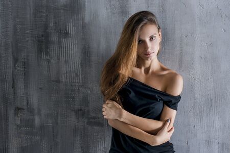 Beautiful young woman in grey shirt and black skirt on dark grey wall backgroundの写真素材