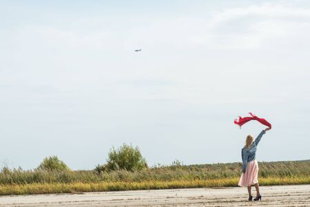 Stylish slender woman, waving his hand flying aircraft in summer Sunny day. Travel, vacation, concept of adventures.の写真素材