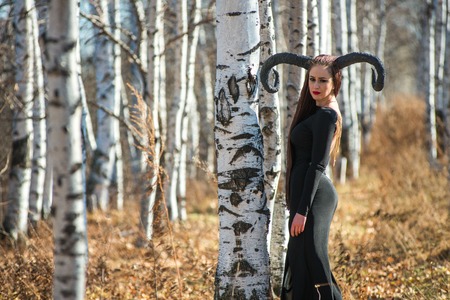 beautiful woman dressed as a fairy witch in raincoat and with horns for Halloweenの写真素材