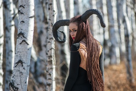 beautiful woman dressed as a fairy witch in raincoat and with horns for Halloweenの写真素材