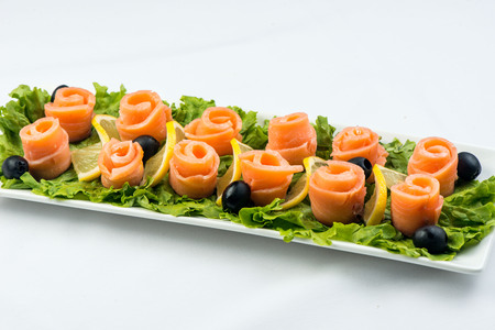 salmon snack on lettuce leaf with lemon and olives on white plate on white backgroundの写真素材