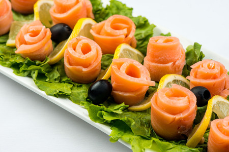 salmon snack on lettuce leaf with lemon and olives on white plate on white backgroundの写真素材