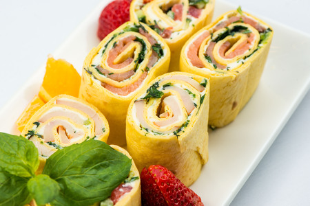 Rolls of thin pancakes with smoked salmon, horseradish cream cheese and rocket leaves on white plate on white backgroundの写真素材