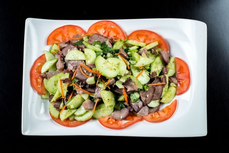 Chinese cuisine, boiled beef with cucumber and tomato in white plate on black backgroundの写真素材