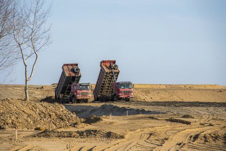 dump truck unloading sand Two red dump trucks unload the soilの写真素材