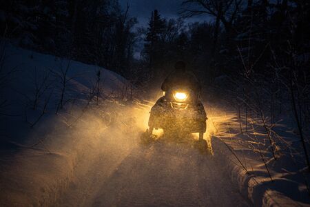 snowmobile in the evening goes through the winter forest. headlights. night road through the winter...