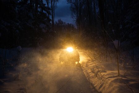 snowmobile in the evening goes through the winter forest. headlights. night road through the winter...