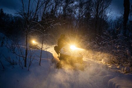 snowmobile in the evening goes through the winter forest. headlights. night road through the winter forest. snowmobile at night.の写真素材