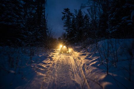 snowmobile in the evening goes through the winter forest. headlights. night road through the winter forest. snowmobile at night.の写真素材