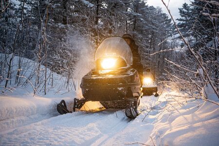 snowmobile in the evening goes through the winter forest. headlights. night road through the winter forest. snowmobile at night.の写真素材