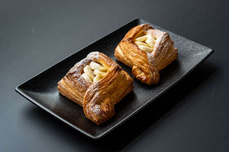 dessert is a small puff pastry pie with stuffing inside on a black serving plate on a black...