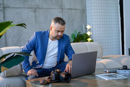 Bearded young confident guy stand behind office desk with laptop thinking working alone. handsome male in casual wear engaged in office work, planning strategy, deadlines. at workplaceの写真素材