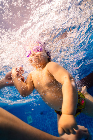 Little child swims underwater in swimming pool, happy active dives and has fun under water, kid fitness and sportの写真素材