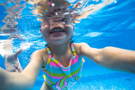 Little child swims underwater in swimming pool, happy active dives and has fun under water, kid fitness and sportの写真素材