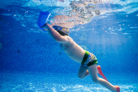 Little child swims underwater in swimming pool, happy active dives and has fun under water, kid fitness and sportの写真素材