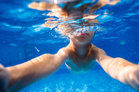 Little child swims underwater in swimming pool, happy active dives and has fun under water, kid fitness and sportの写真素材