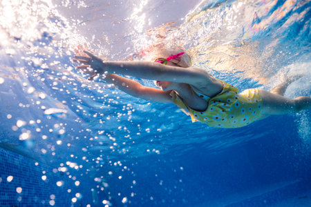 Little child swims underwater in swimming pool, happy active dives and has fun under water, kid fitness and sportの写真素材