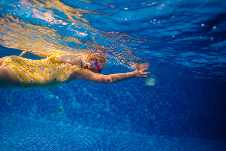 Little child swims underwater in swimming pool, happy active dives and has fun under water, kid fitness and sportの写真素材