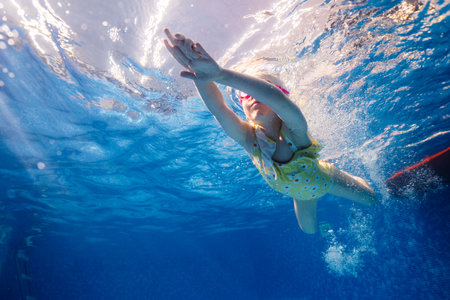 Little child swims underwater in swimming pool, happy active dives and has fun under water, kid fitness and sportの写真素材