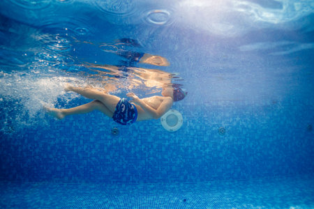 Little child swims underwater in swimming pool, happy active dives and has fun under water, kid fitness and sportの写真素材
