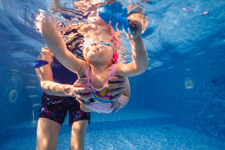 Little child swims underwater in swimming pool, happy active dives and has fun under water, kid fitness and sportの写真素材