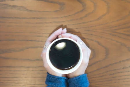 Woman hand with cloth hold a cup of black coffee on brown wood table.の写真素材