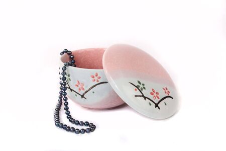 A pink porcelain jewelry box and black pearls, isolated on white background.の写真素材