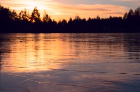 A small lake in winter, frozen across the top with clear ice, at sunset.の写真素材