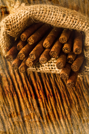 cigar in small sack on the old wooden table overlap with old wall textured background. retro filter.