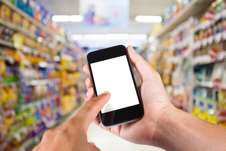Person using smartphone white screen holder on hand with shelves on background in supermarket.の写真素材