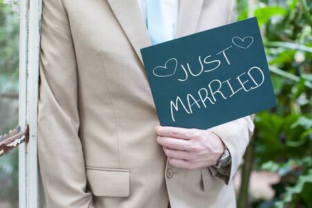 Groom holding small blackboard with message Just Marriedの写真素材