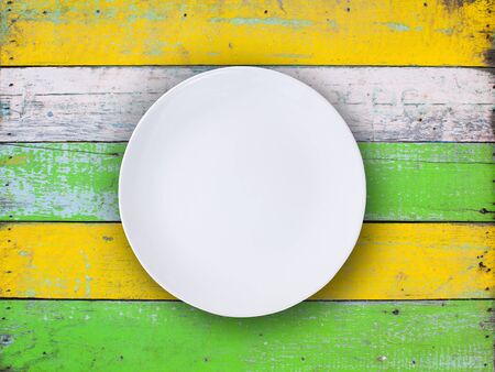 Top view of empty white plate put on colorful wood table with space for copy.の写真素材