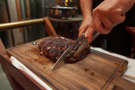 Cutting grill beef on wooden cutting board in the restaurant for dinner.の写真素材