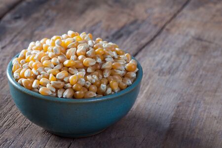 Dry corn kernels in a green bowl, set on a wooden table.