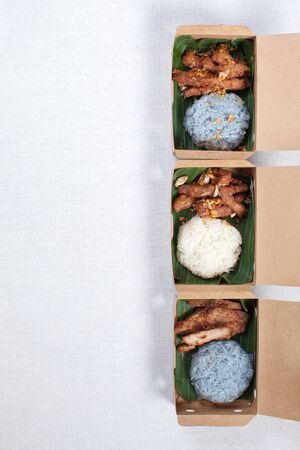 Sticky rice with grilled pork and fried pork put in a brown paper box, put on a white tablecloth, food box, Thai food.の写真素材