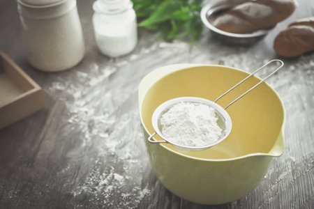 Sieve flour on yellow mixing bowl and bakery ingredients.の写真素材