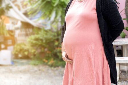 Photo of pregnant belly in nature. Pregnant woman in dress holds hands on belly on natural backgroundの写真素材