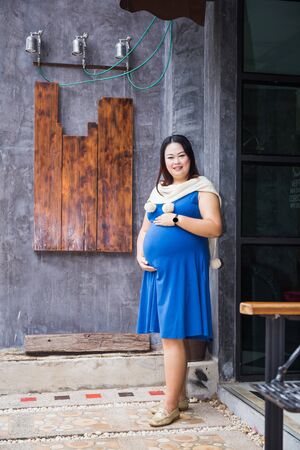 Photo of pregnant belly. Pregnant woman in dress holds hands on belly on wall background.の写真素材