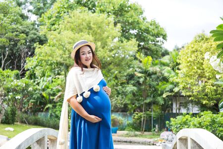 Photo of pregnant belly in nature. Pregnant woman in dress holds hands on belly on natural backgroundの写真素材