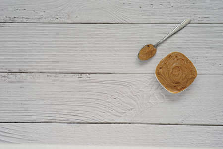 Peanut butter in a white ceramic cup placed on white wooden background, copy space concept.の写真素材