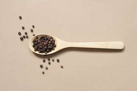 top view selective focus at dried peppercorns poured on brown wooden spoon placed on brown paper background.の写真素材
