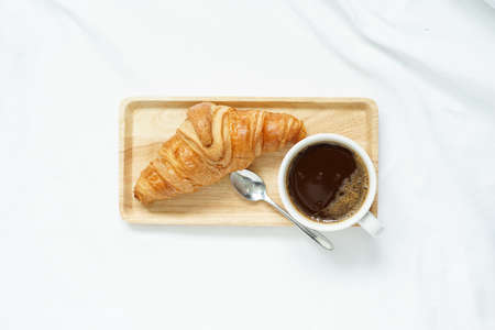breakfast in bed concept with top view of fresh croissant served with hot coffee cup in white...