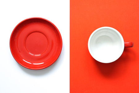top view of empty round red ceramic mug and red round ceramic saucer  placed on two tone colour of white and red background with beautiful light in the morning,conceptual of  porcelain mockup for advertising.の写真素材