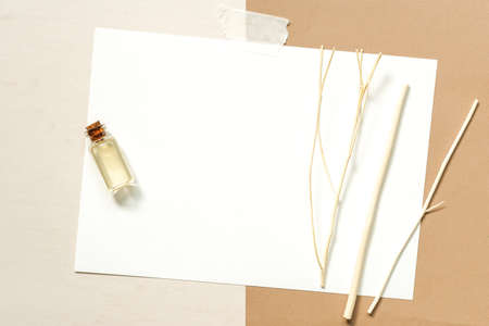 Top view of essential oils in a small transparent glass bottles and diffuser reeds sticks placed on blank white mock up card placed on beige and brown background.の写真素材