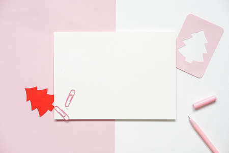 Blank white paper with paper cut in the shape of a Christmas tree and pink pen set on white paper and pink paper background, greetings card ideas for the Christmas seasonの写真素材