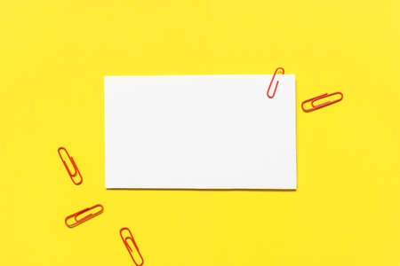 blank white paper with red paper clips on yellow paper background.の写真素材