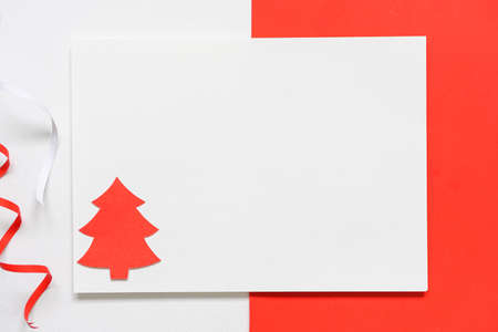 Blank white paper with paper cut in the shape of a Christmas tree and color paper ribbons set on white paper and red paper background, greetings card ideas for the Christmas seasonの写真素材