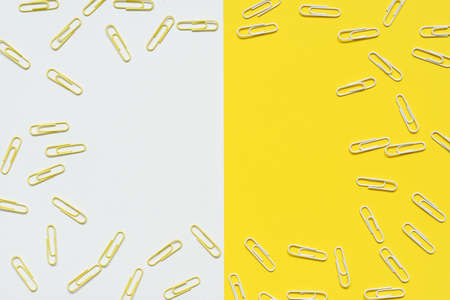 White and yellow paper clips are spilled over empty yellow and white paper in this top view.blank...