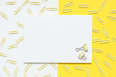 top view of blank white A4 paper with yellow and white paperclips spilled over a yellow and white paper background.の写真素材